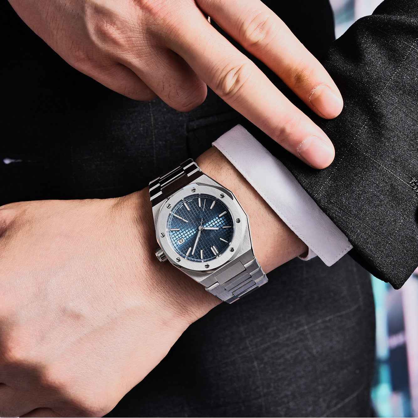 Close-up of a wrist wearing a silver watch with a blue face, against a blurred background.