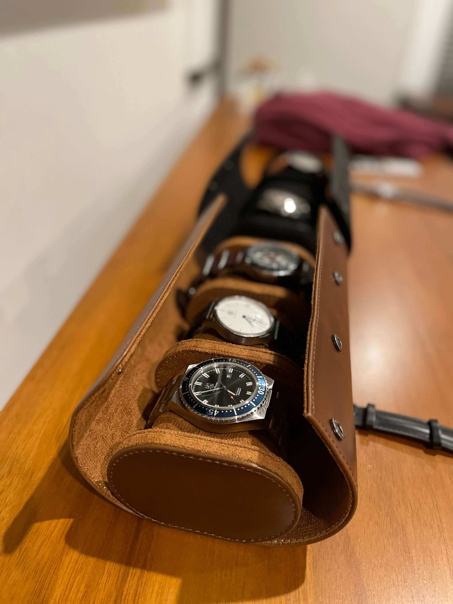 Brown leather watch holder with watches on a wooden surface